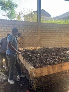 Workers turning compost in a wooden composting box under a shelter